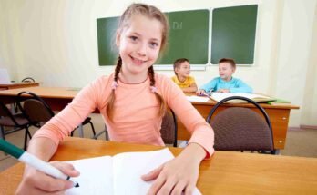 A young girl taking an 11 Plus Mock Exam at a desk in a classroom, with other students in the background.